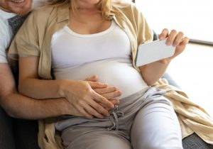 gravida abraçada com outra pessoal enquanto segura celular
