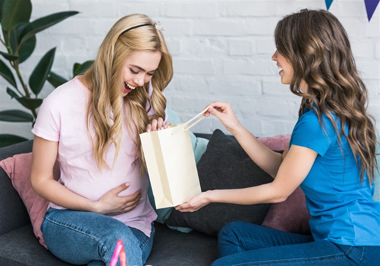 Mulher gravida no sofa recebendo presente de amiga